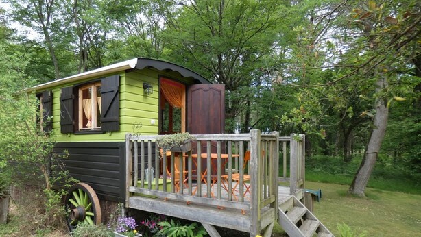 A green and black mobile home with a wooden deck and outdoor seating area. - La Roulotte - Leon - Roulotte (LEON)