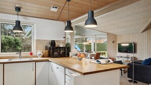 A modern kitchen with a wooden countertop, white cabinets, and a built-in dishwasher. There is a large window providing a view of the outdoors, and a dining area with a TV and seating. - Lovely home in Vejby with kitchen (Vejby)