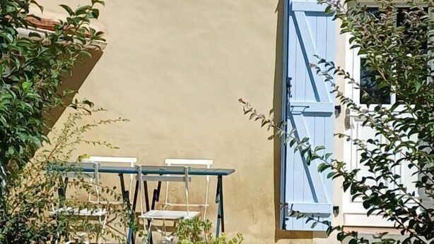 A building with a beige facade, a blue door, and a small garden area with potted plants and a table.