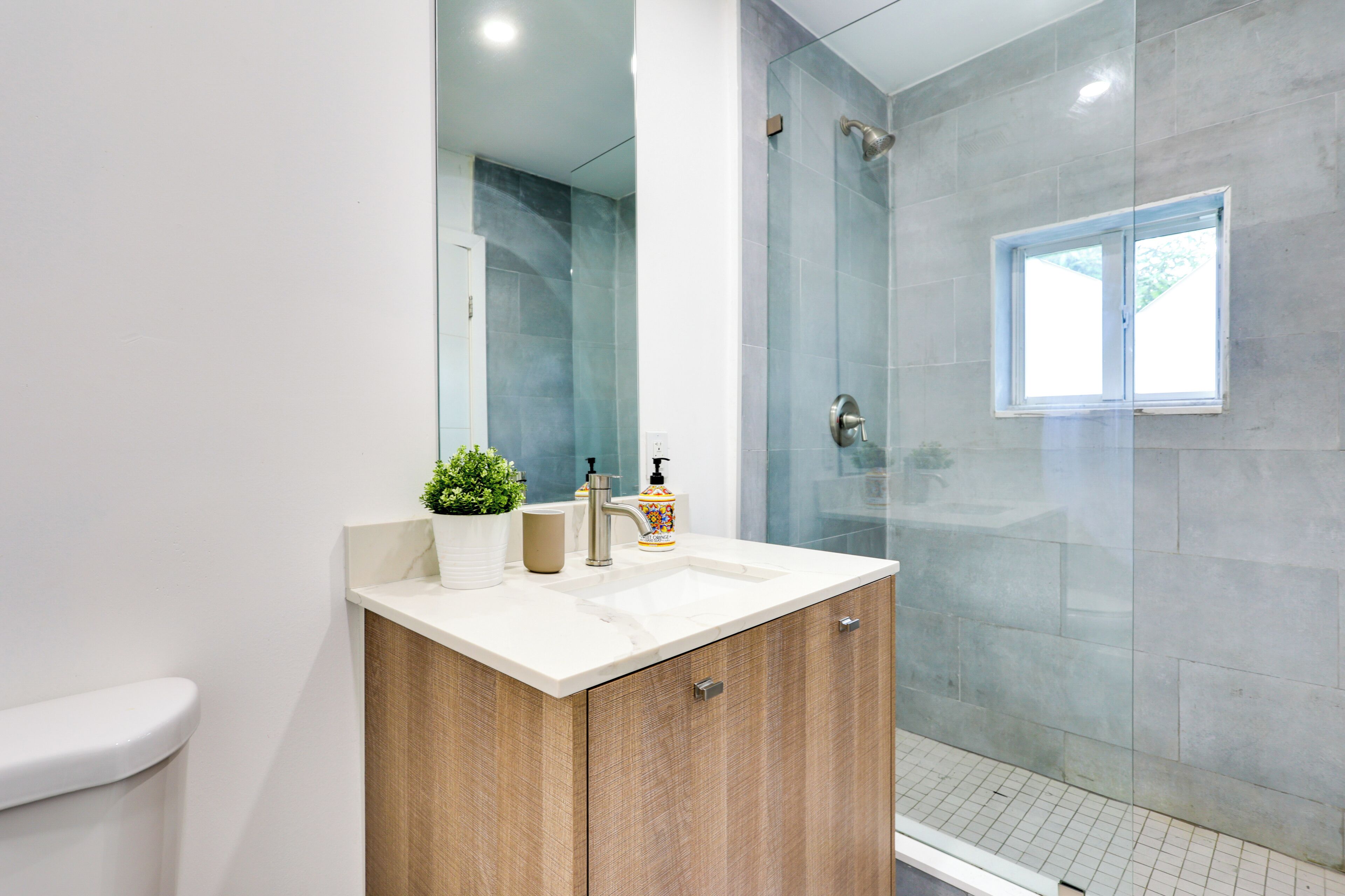 A modern bathroom with a wooden vanity, a white sink, and a glass shower enclosure.