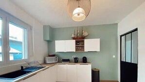 Een kleine keuken met witte kastjes, een magnetron, een waterkoker en een spoelbak.
