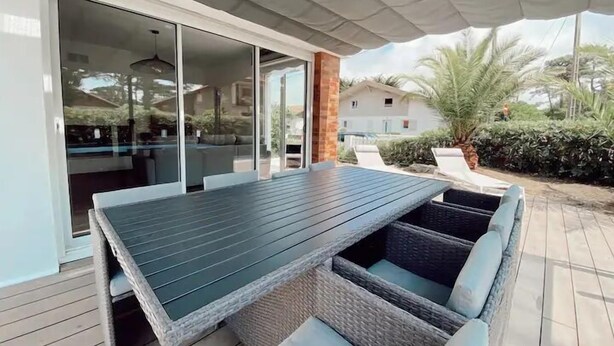 Een terras buiten met een tafel, stoelen, een schuifpui en uitzicht op de omgeving.