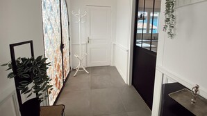 Een gang met een witte deur, een plant, een ingelijst schilderij en een hanglamp.