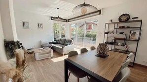 Een moderne woonkamer met een bank, eettafel en stoelen. Er is een groot raam dat natuurlijk licht en uitzicht biedt.