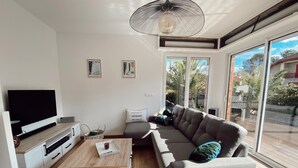 Een moderne woonkamer met een flatscreen-tv, een grijze bank, een houten salontafel en een groot raam met uitzicht op palmbomen.