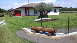 A fenced garden area with a wooden bench, a tree, and a building in the background. - Jouanon - Bias - Gîte (BIAS)