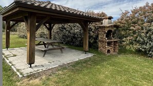 A wooden gazebo with a picnic table, surrounded by a garden with flowering bushes. - Jouanon - Bias - Gîte (BIAS)