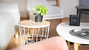 Ein modernes Wohnzimmer mit einem weißen Sofa, einem runden Couchtisch mit einer Pflanze, einem weißen Sessel, einem Holznachttisch und einem gerahmten Kunstwerk an der Wand.