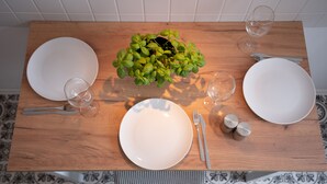 Ein Holzespeisetisch mit weißen Tellern, Besteck und Gläsern, in der Mitte ein Blumentopf.