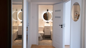 Ein modernes Badezimmer mit Toilette, Waschbecken und Badewanne, mit einem runden Spiegel über dem Waschbecken und einem gefliesten Boden.