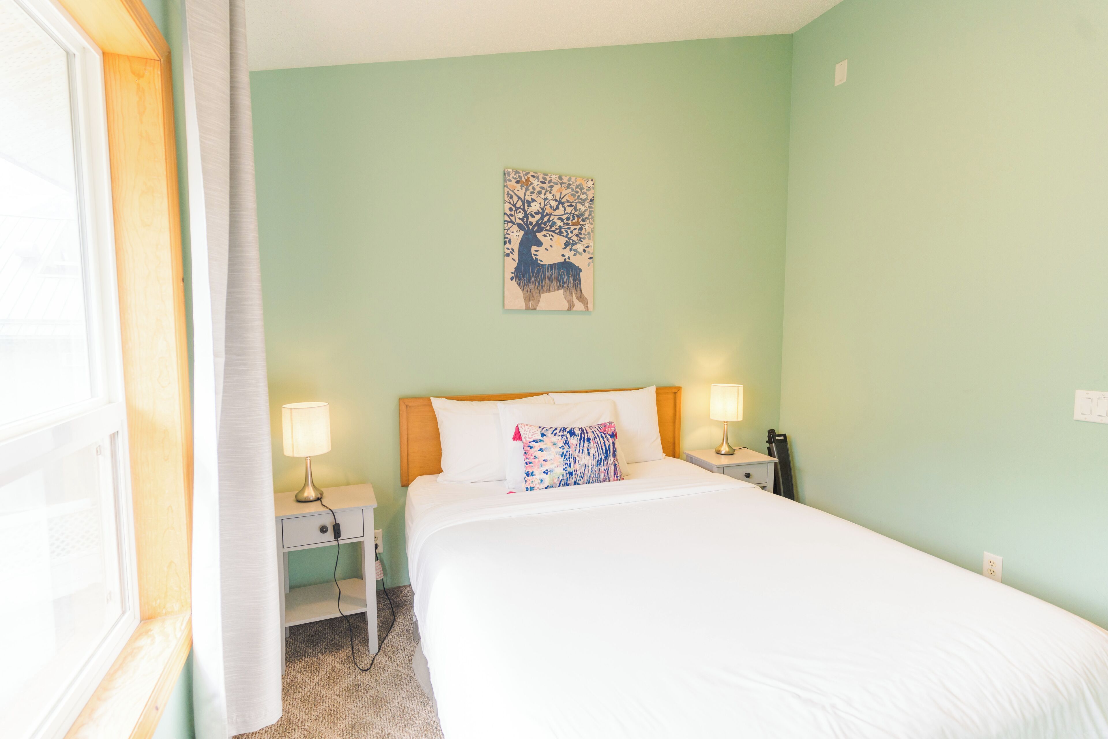 Quarto com uma cama, duas mesas de cabeceira, um criado-mudo, uma luminária e uma pintura de um veado na parede.