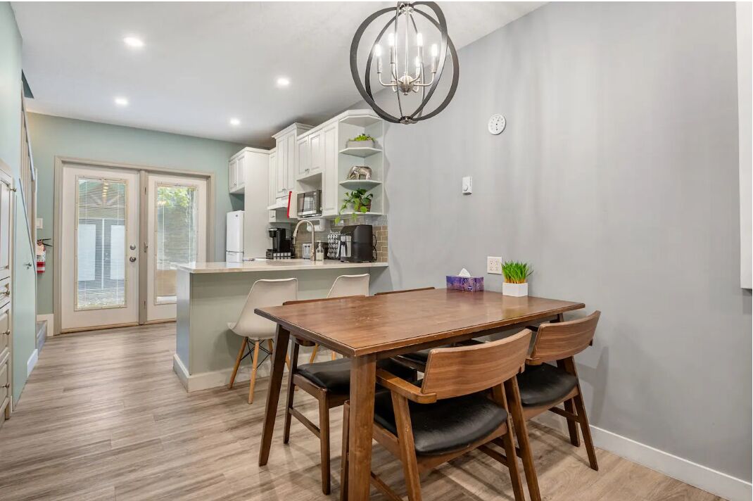 Une cuisine moderne avec des meubles blancs, un îlot central et un coin repas comprenant une table et des chaises en bois.