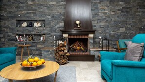 Una sala de estar con chimenea de piedra, sofás color aguamarina, una mesa de centro de madera con naranjas, y un reloj sobre la chimenea.