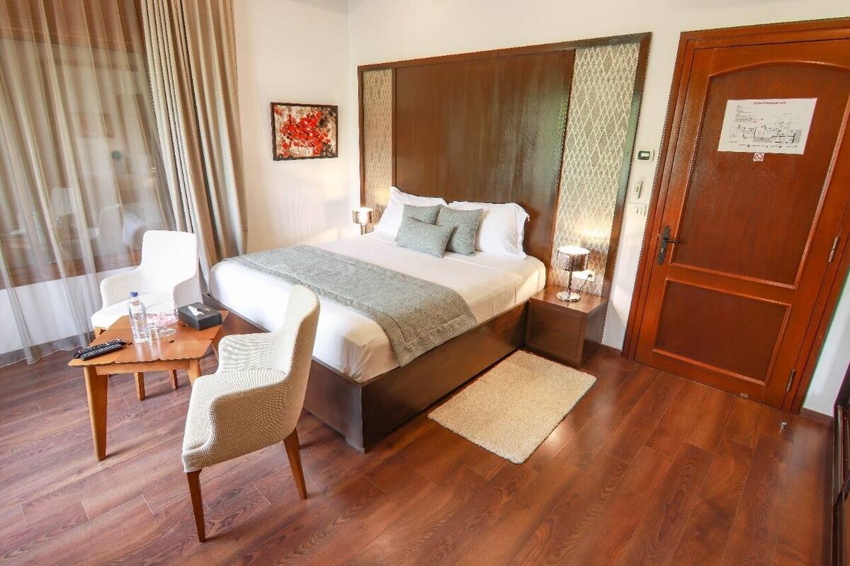 Una habitación de hotel con una cama grande, un cabecero de madera, un escritorio con una silla, una mesita y una puerta con un cartel.