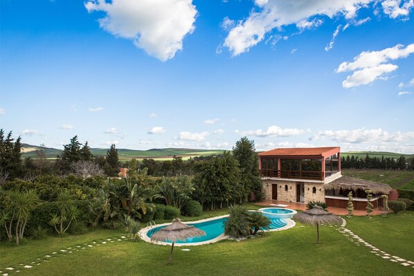 Une maison moderne avec une piscine, entourée d’une végétation luxuriante et sous un ciel d’un bleu éclatant.