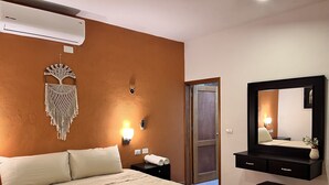 Een hotelkamer met een bed, een macramé decoratie aan de muur, een wandlamp, een telefoon naast het bed, een spiegel en een kleine tafel.