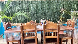 Een houten eettafel met vier stoelen, op de achtergrond een groene haag.
