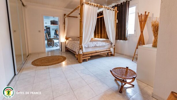 A bedroom with a four-poster bed, a wicker chair, and a small rug.