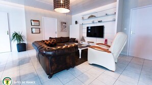 A modern living room with a leather sofa, a white armchair, a TV on a shelf, and a potted plant.