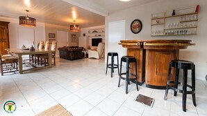 A spacious living area with a wooden dining table, black bar stools, and a bar counter.
