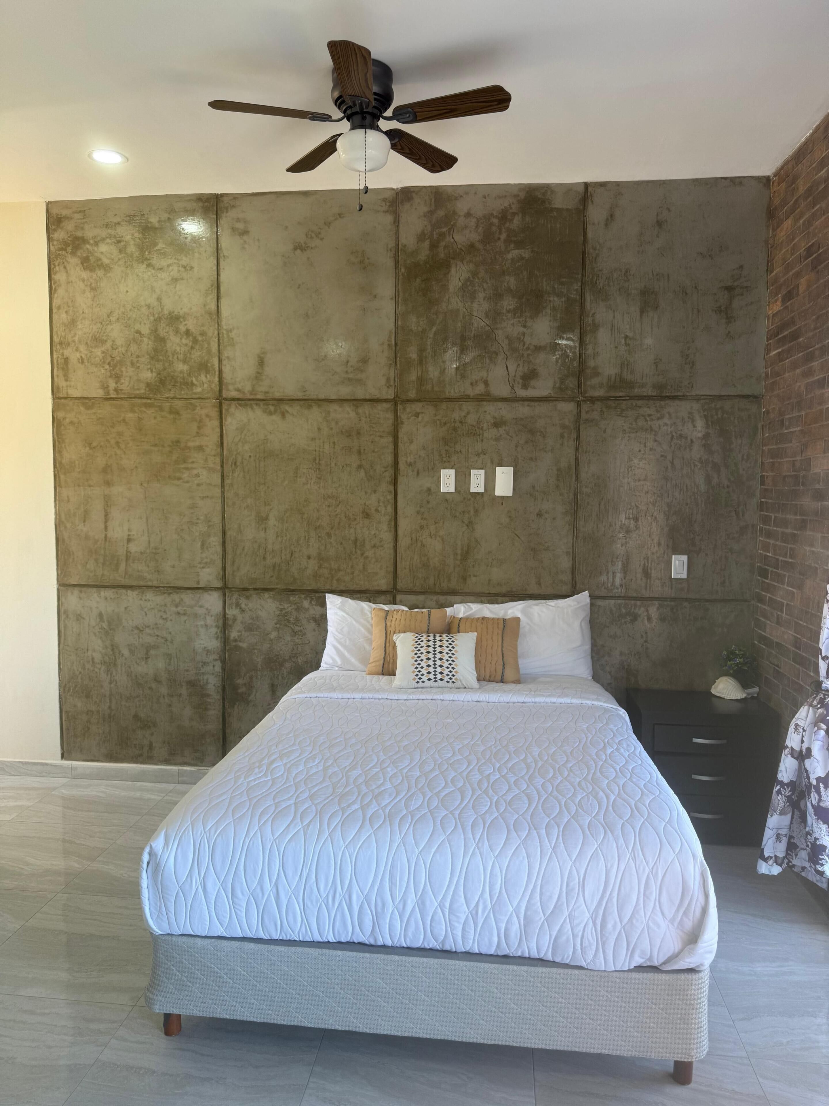 Een slaapkamer met een groot bed, een plafondventilator en een bakstenen muur.