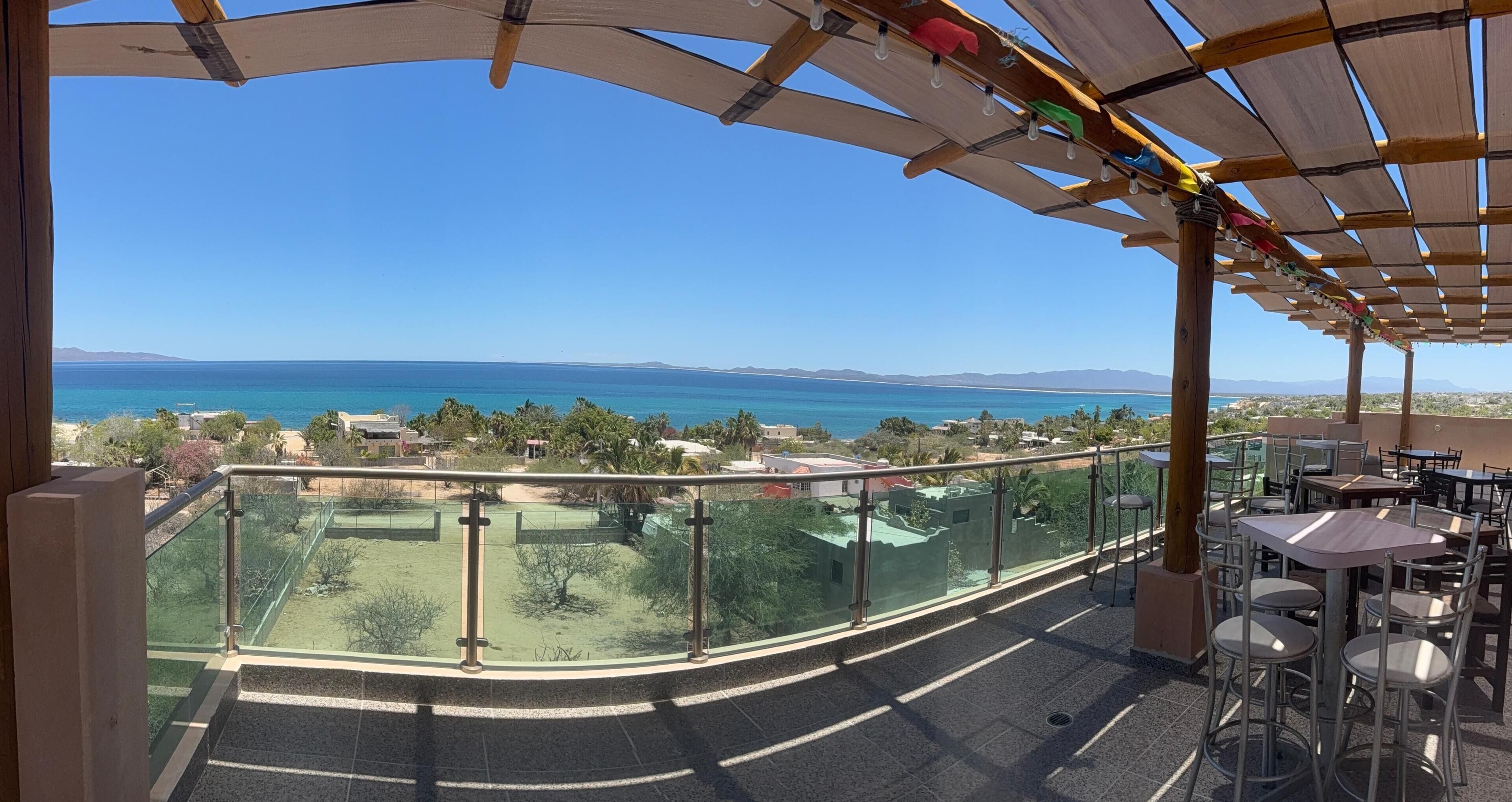 Un balcon avec vue sur la mer, un espace extérieur aménagé et couvert, et une balustrade en verre.