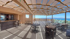 Eine Terrasse im Freien mit Tischen, Stühlen, einer Bar und Blick aufs Meer.