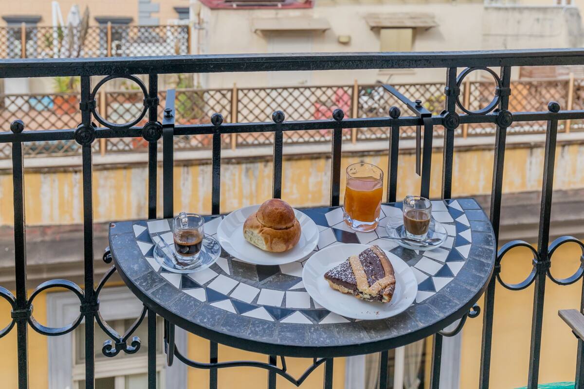 A table with a meal and drinks on a balcony overlooking a cityscape with a prominent dome building.