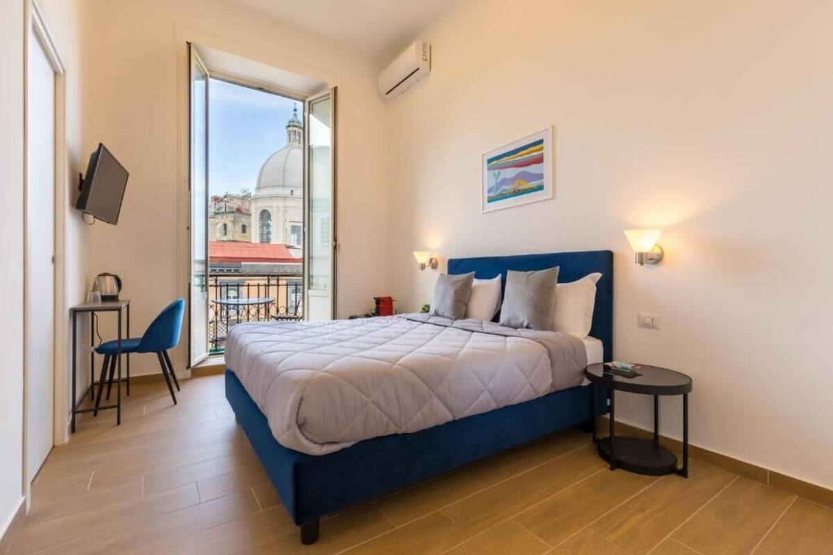 A bedroom with a bed, a small table, a chair, and a view of a building through a glass door.