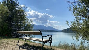 A bench by a lake with mountains in the background. - Wunderschöne, Moderne Ferienwohnung in Österreich mit dem Charme von 1750 (Feistritz im Rosental)