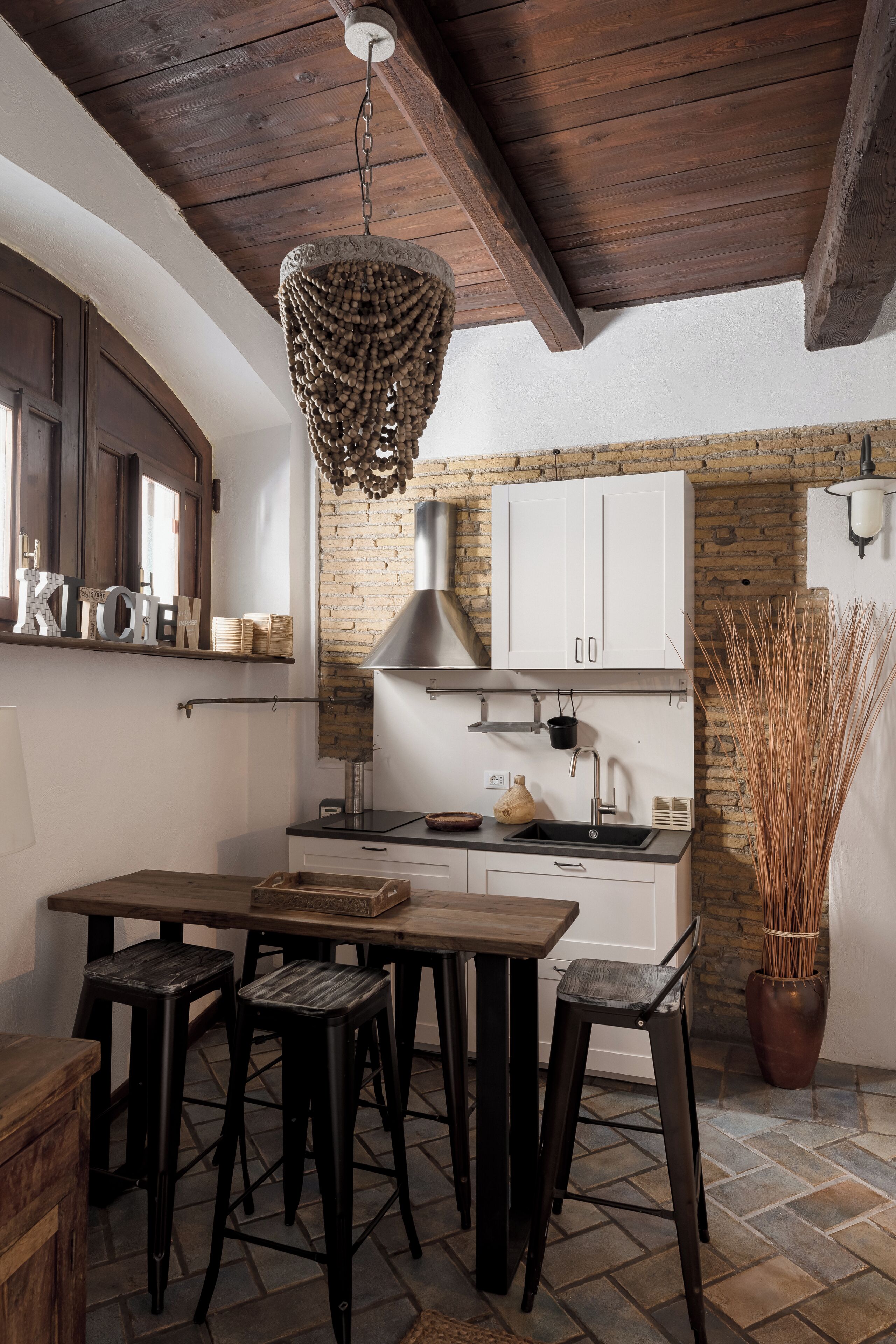 A kitchen with a wooden ceiling, white cabinets, a hanging light fixture, and a potted plant.