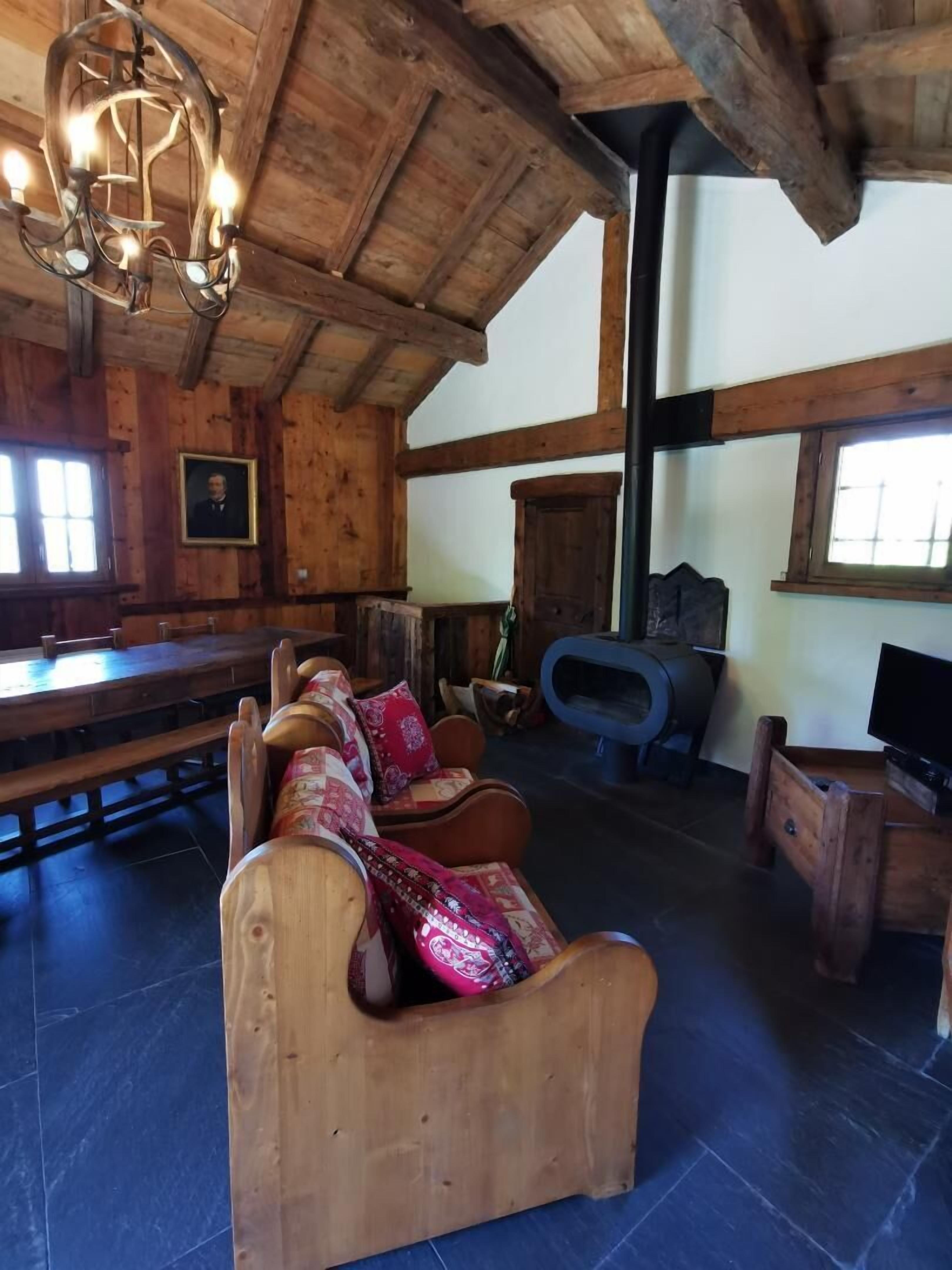 Un intérieur rustique avec des éléments en bois, notamment un long banc en bois, un canapé confortable agrémenté de coussins à motifs, un téléviseur posé sur un meuble en bois et une cheminée.