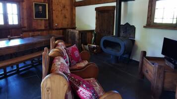 Un intérieur rustique avec des éléments en bois, notamment un long banc en bois, un canapé confortable agrémenté de coussins à motifs, un téléviseur posé sur un meuble en bois et une cheminée.