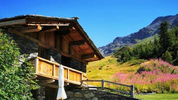 Un chalet rustique avec une façade en pierre, un balcon en bois et un espace extérieur aménagé avec des chaises et une table.