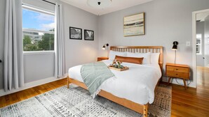 A bedroom with a large bed, a window with curtains, a headboard, bedside tables, and a painting on the wall. - Spacious Stadium District 2BR King Bed (Tacoma)