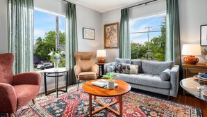 A living room with a sofa, armchair, and coffee table, large windows with curtains, and a view of greenery outside. - Spacious Stadium District 2BR King Bed (Tacoma)