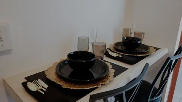 Taula de menjador preparada amb bols, plats i coberts negres, acompanyats d'una espelma i un got.