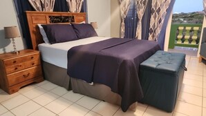 Un dormitori amb llit, taula de nit i un petit otomà.