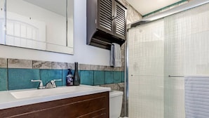 Un baño con un lavabo blanco, un espejo, una toalla colgada en un perchero y una ducha con puerta de vidrio.
