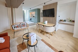 Un salon moderne avec un coin repas, un téléviseur fixé sur un panneau en bois et une cuisine en arrière-plan.