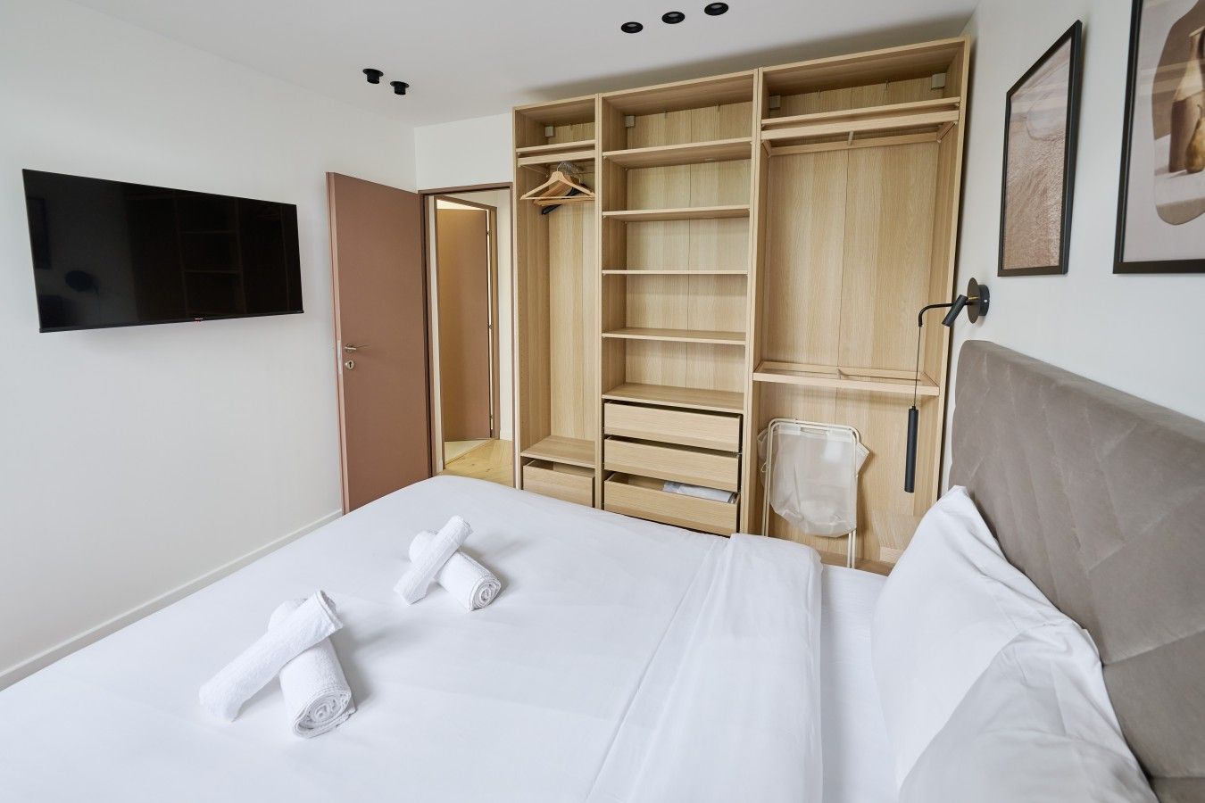 A hotel room with a bed, a large wardrobe, a television, and a towel rack.