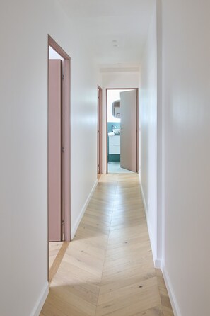 Un couloir doté d’un plancher en bois et de murs blancs, qui mène à une salle de bain avec des toilettes et un lavabo.