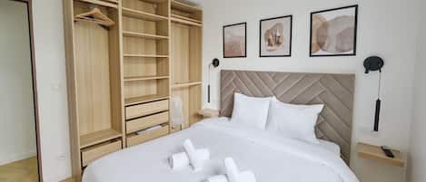 Une chambre d’hôtel avec un grand lit, une armoire avec plusieurs étagères, une table de chevet avec une lampe et des œuvres d’art accrochées au mur.
