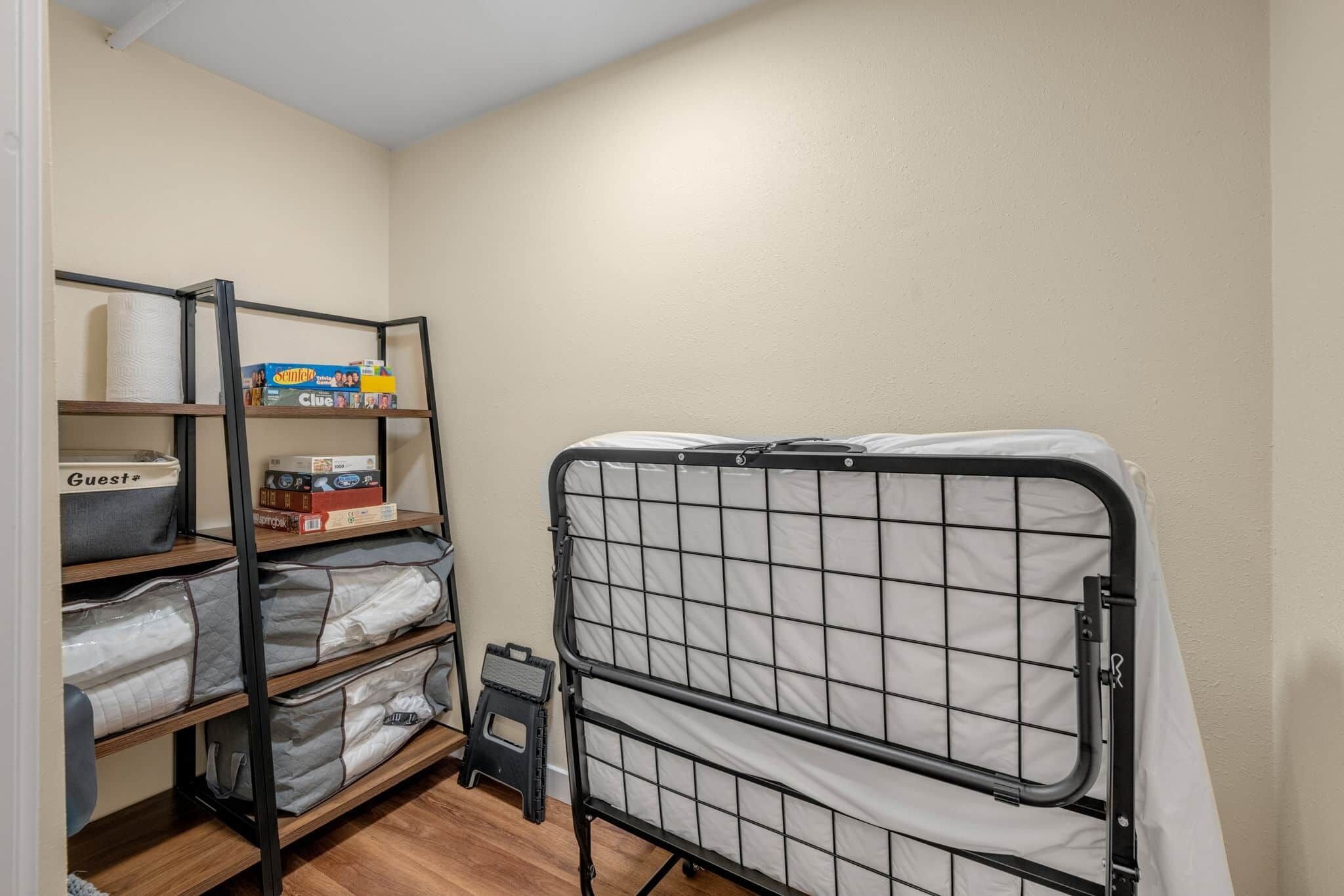 Una habitación pequeña y ordenada con una cama litera, estanterías con cajas de almacenamiento y un taburete.