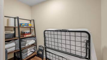 Una habitación pequeña y ordenada con una cama litera, estanterías con cajas de almacenamiento y un taburete.