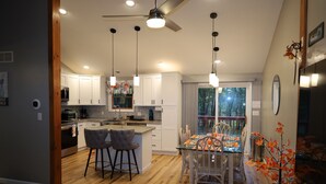 Une cuisine moderne avec des meubles blancs, un îlot central, des tabourets de bar et des luminaires suspendus.