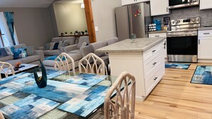 Une cuisine moderne équipée d’appareils électroménagers en acier inoxydable, un coin repas avec une table en verre et un salon agrémenté d’un canapé et de coussins décoratifs.