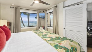 Une chambre d’hôtel avec un lit, un ventilateur de plafond, une vue sur l’océan et une porte fermée.