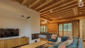 Una sala de estar moderna con televisor, muebles de madera, un sofá y un comedor con sillas y mesa.
