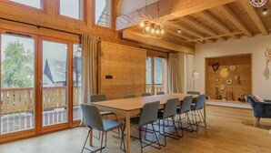 Una habitación espaciosa con una gran mesa y sillas de madera, ventanas amplias y techo de madera.